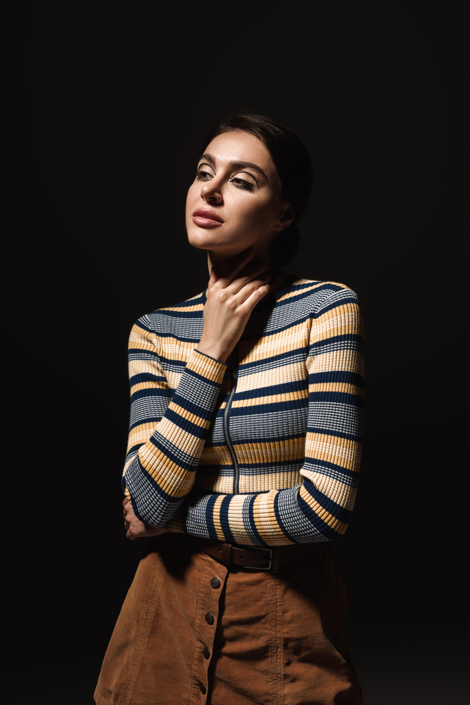 dreamy young woman in striped turtleneck and skirt looking away isolated on black  - Photo, Image