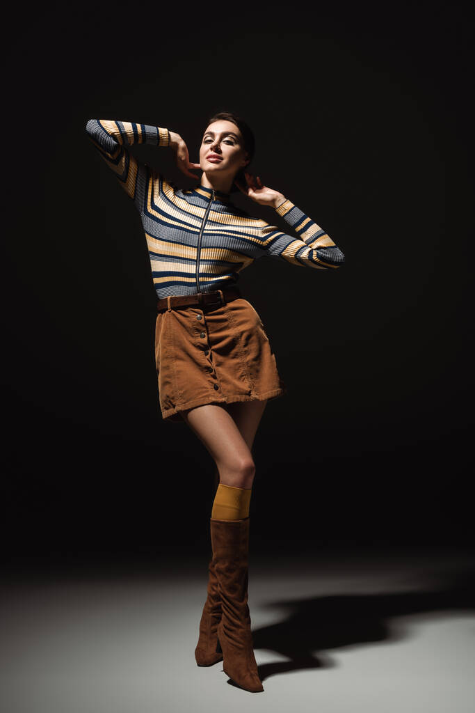 full length of pretty young woman in striped turtleneck with skirt and boots posing on black  - Photo, Image
