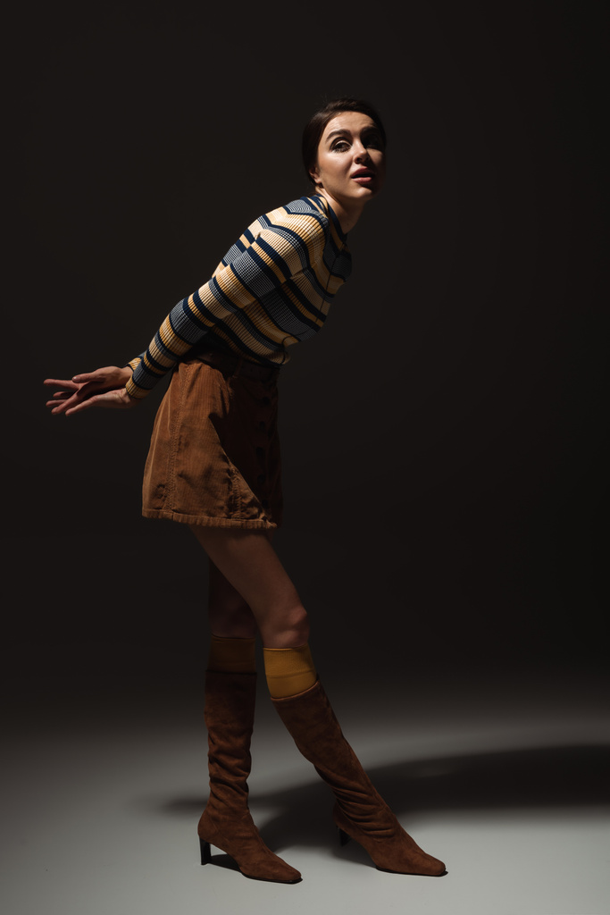 full length of young model in striped turtleneck with skirt and boots posing on black  - Photo, Image