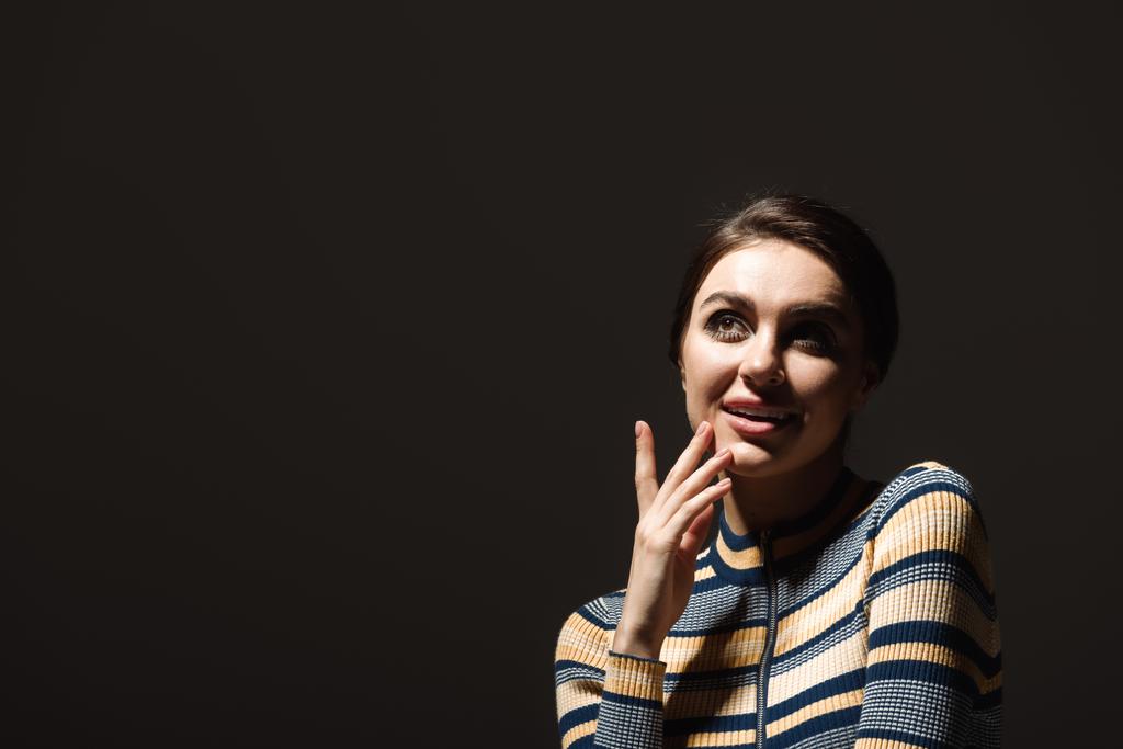 pleased young woman in striped turtleneck looking away isolated on black  - Photo, Image