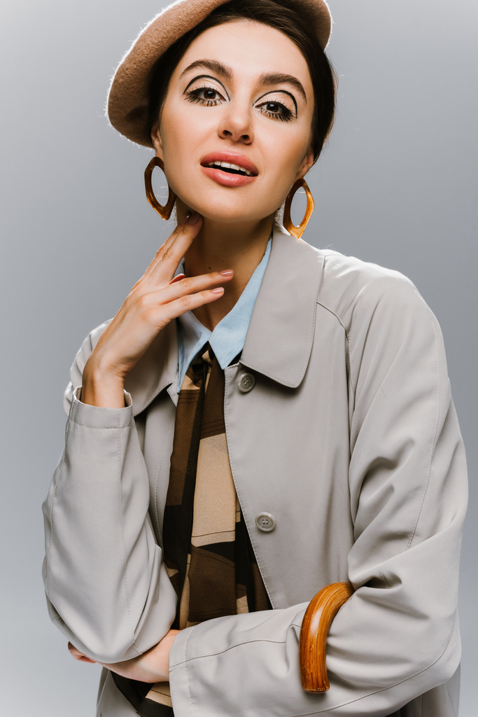 portret van pin up jonge vrouw in baret en trench jas poseren geïsoleerd op grijs - Foto, afbeelding