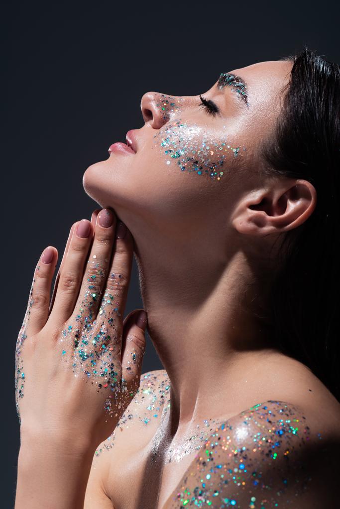 side view of young woman with closed eyes and glitter on face praying isolated on grey - Photo, Image