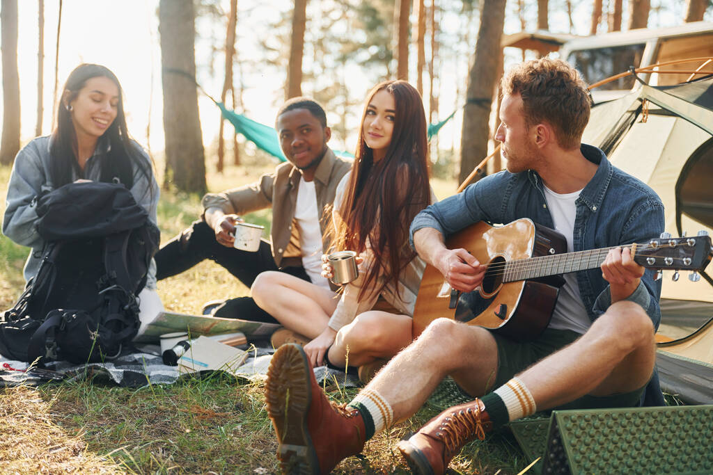 El hombre toca la guitarra. Grupo de jóvenes viaja juntos en el bosque durante el día. - Foto, Imagen
