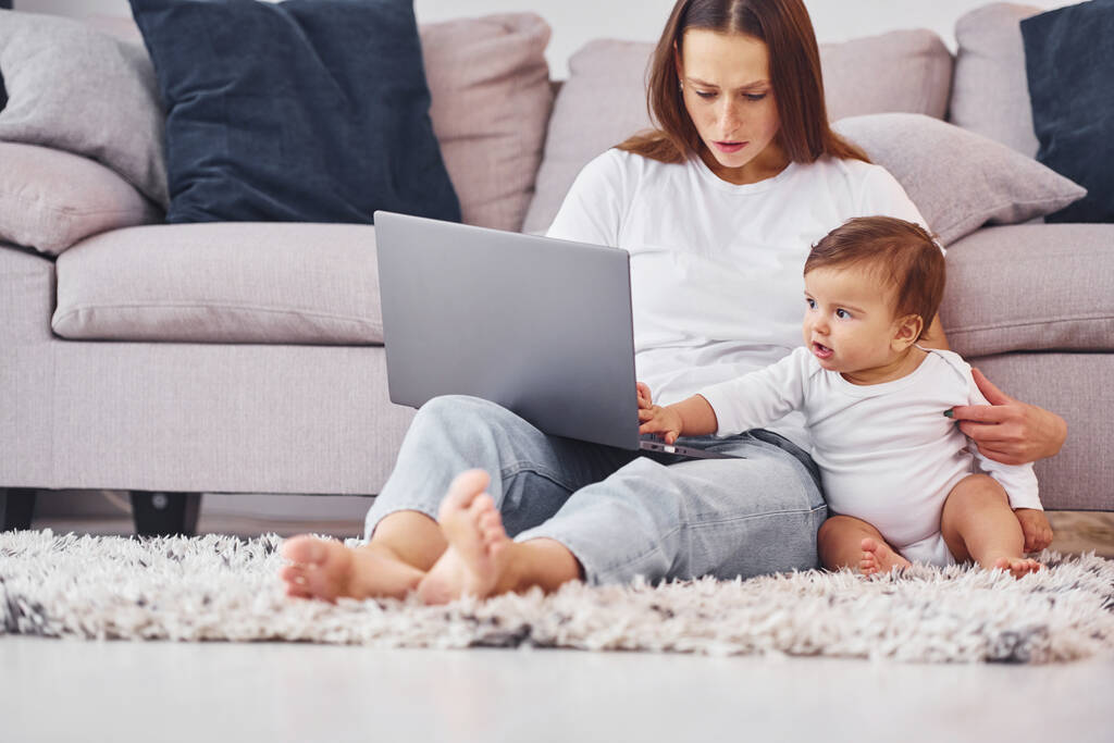Using laptop. Mother with her little daughter is indoors at home together. - Photo, Image