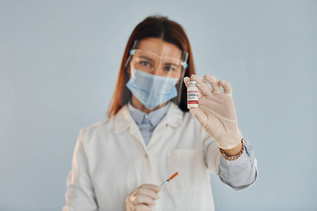 Fiatal nő orvos fehér köpenyben áll beltérben ellen kék háttér. - Fotó, kép