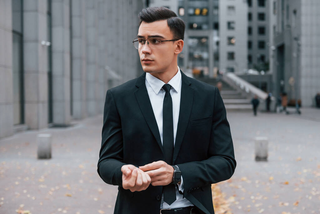 Porträt eines Geschäftsmannes in schwarzem Anzug und Krawatte steht draußen in der Stadt. - Foto, Bild