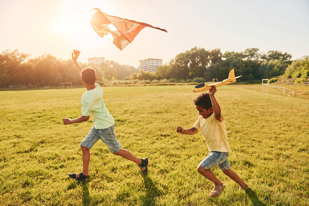 Running with kite. Two african american kids have fun in the field at summer daytime together. - Photo, Image