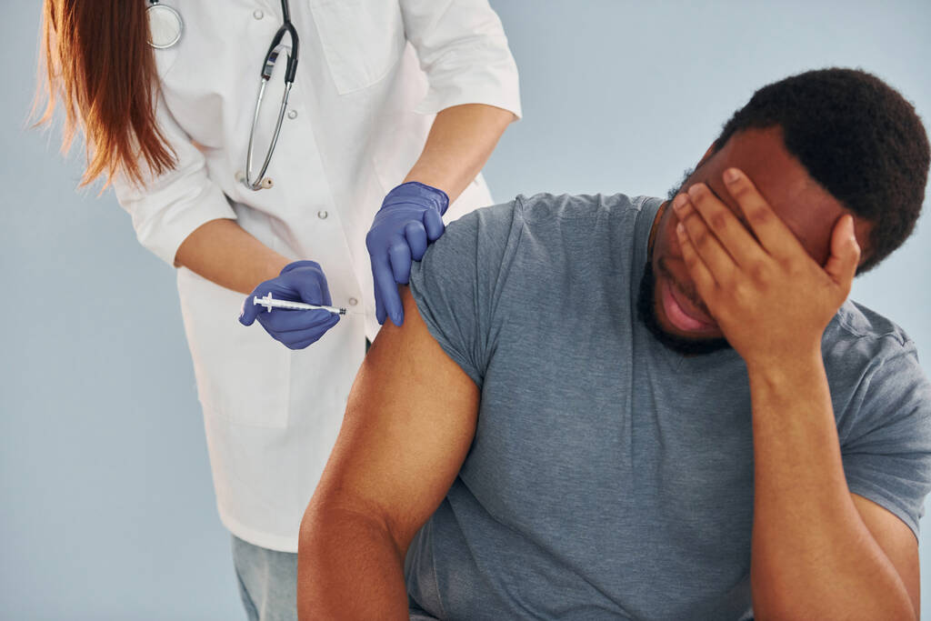 Vrouwelijke arts geeft injectie aan Afrikaans-Amerikaanse man in het ziekenhuis. - Foto, afbeelding