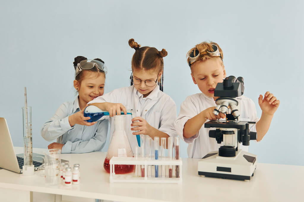 probówki z kolorowym płynem. Dzieci w białych fartuchach bawią się w naukowców w laboratorium używając sprzętu. - Zdjęcie, obraz