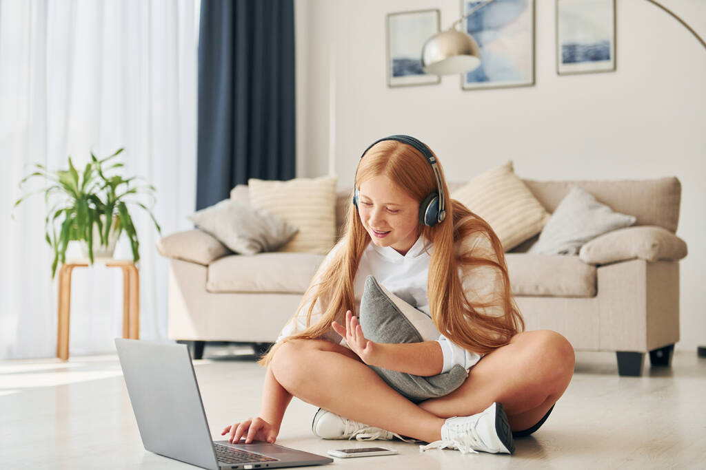 Usando laptop. Adolescente feminina com cabelo loiro está em casa durante o dia. - Foto, Imagem