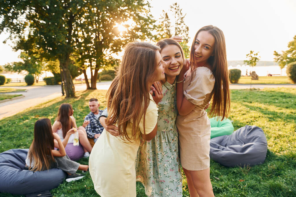 Vrouwen omhelzen elkaar. Groep jongeren geeft overdag een feestje in het park. - Foto, afbeelding
