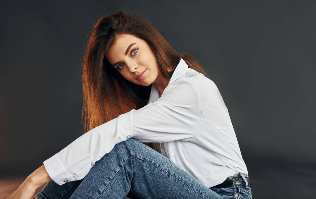 In een wit shirt en een blauwe jeans. jong mooi vrouw is poseren voor de camera in de studio. - Foto, afbeelding