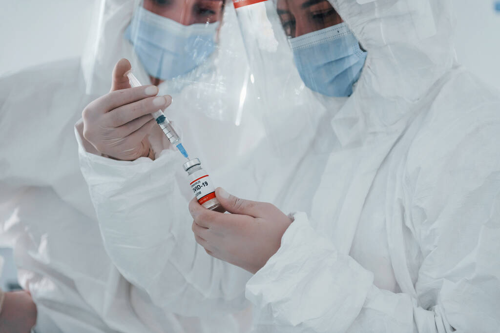 Las trabajadoras médicas en uniforme protector trabajan con la vacuna COVID-19. - Foto, imagen
