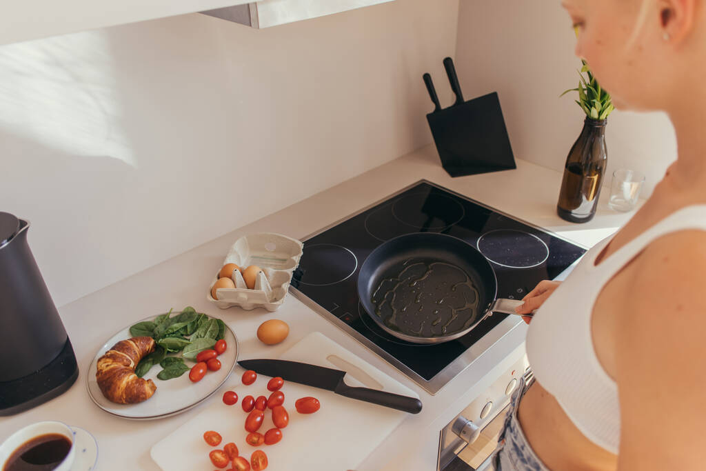 Cropped view of woman in top holding frying pan near cherry tomatoes and eggs in kitchen  - Photo, Image