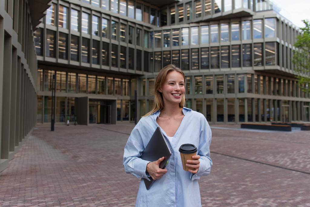 Veselá mladá žena drží notebook a papírový pohár na ulici v Berlíně  - Fotografie, Obrázek