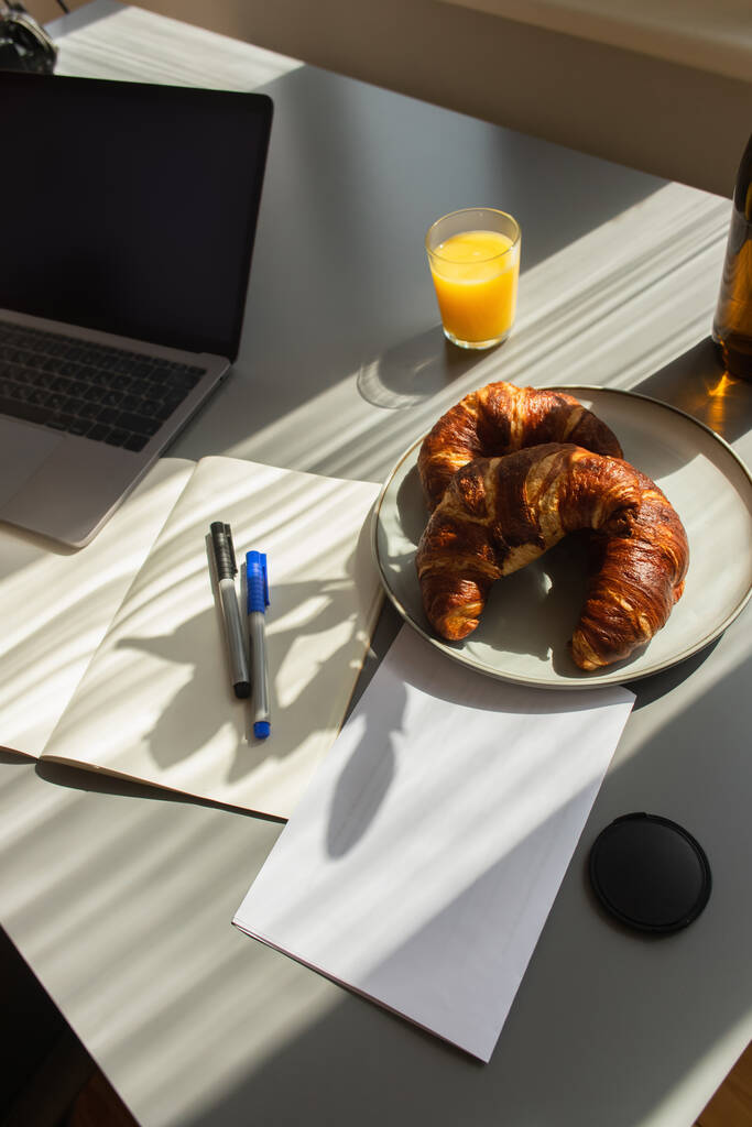 Hoge hoek uitzicht van croissants in de buurt van laptop en sinaasappelsap op tafel thuis  - Foto, afbeelding