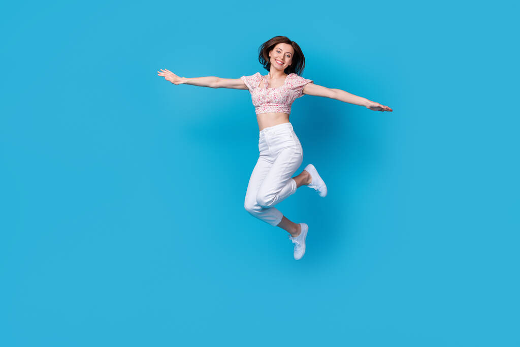 Foto de linda dama positiva vestida traje de moda saltando mostrando brazo imaginar puede volar espacio vacío aislado sobre fondo de color azul. - Foto, Imagen