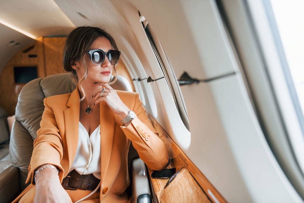 In een zonnebril. Jonge passagier vrouw in gele kleren vliegt in het vliegtuig. - Foto, afbeelding