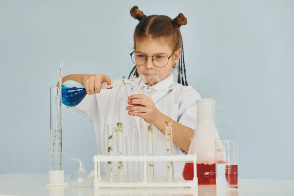 Klein meisje in jas spelen een wetenschapper in het lab met behulp van apparatuur. - Foto, afbeelding