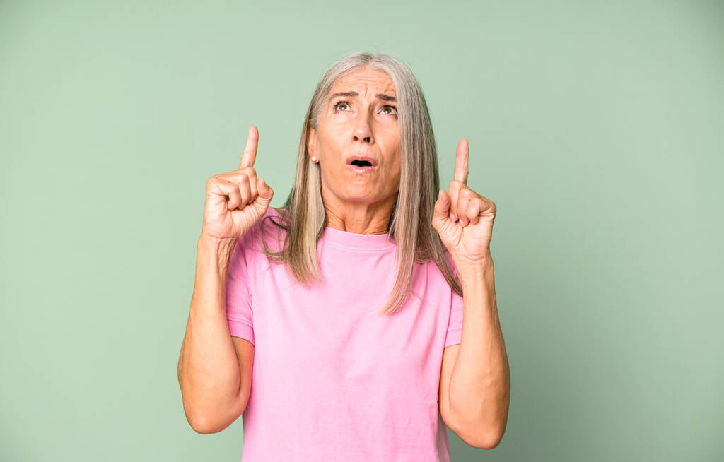 pretty gray hair senior woman feeling awed and open mouthed pointing upwards with a shocked and surprised look - Photo, Image