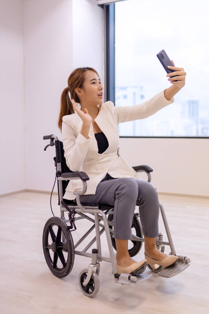 Офісні працівниці жінка на інвалідному візку в яскравому офісі і тримає смартфон
. - Фото, зображення
