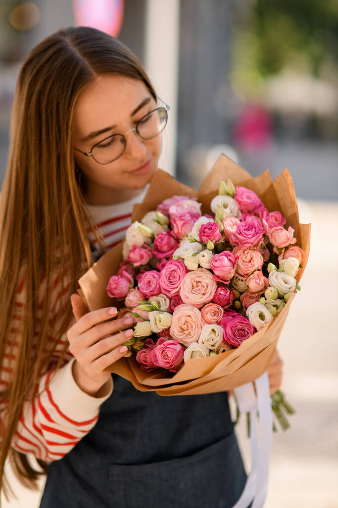 krásná mladá žena něžně drží kytice růžové růže květiny v balicím papíru a podívejte se na to - Fotografie, Obrázek