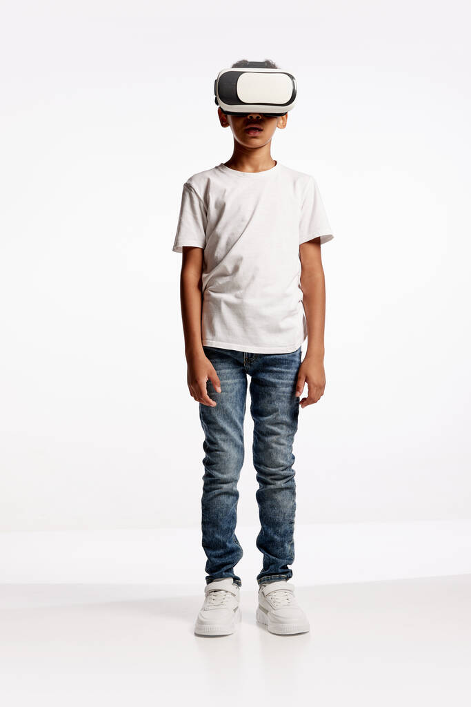 Chłopiec w wieku szkolnym w stroju casual stylu korzystających technologii 3D w wirtualnej rzeczywistości słuchawki izolowane na białym tle. Koncepcja najnowocześniejszej technologii, gier wideo, innowacji i reklamy. - Zdjęcie, obraz