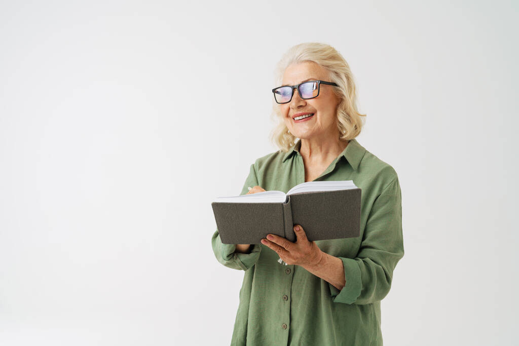 Šedá starší žena v brýlích s úsměvem při pózování s plánovačem izolované přes bílé pozadí - Fotografie, Obrázek