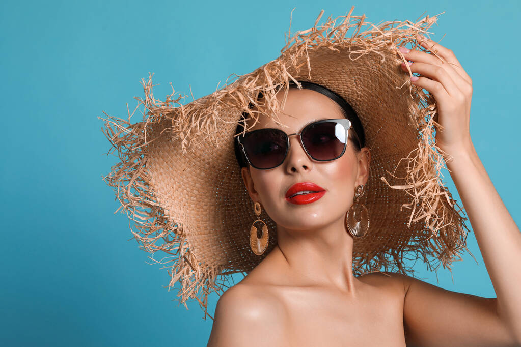 Привлекательная женщина в модных солнечных очках и плетеной шляпе на светло-голубом фоне. Пространство для текста - Фото, изображение