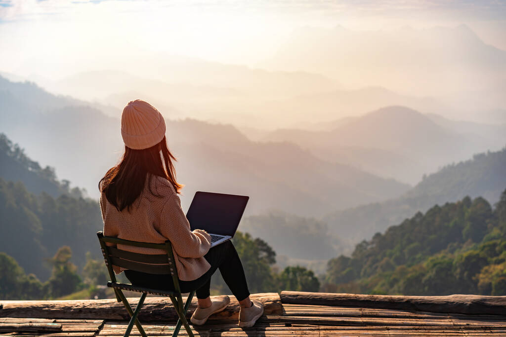 Jovem viajante freelancer trabalhando online usando laptop e desfrutando da bela paisagem da natureza com vista para a montanha ao nascer do sol - Foto, Imagem