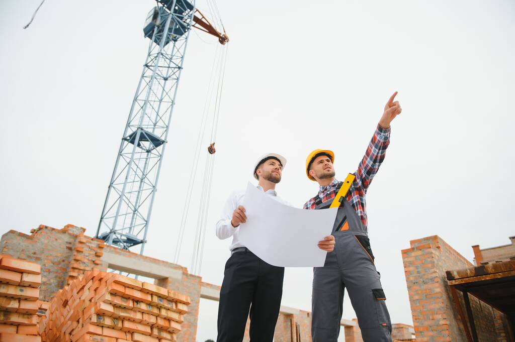 Инженер-строитель и бригадир обсуждают, планируют работу на строительной площадке на открытом воздухе. - Фото, изображение