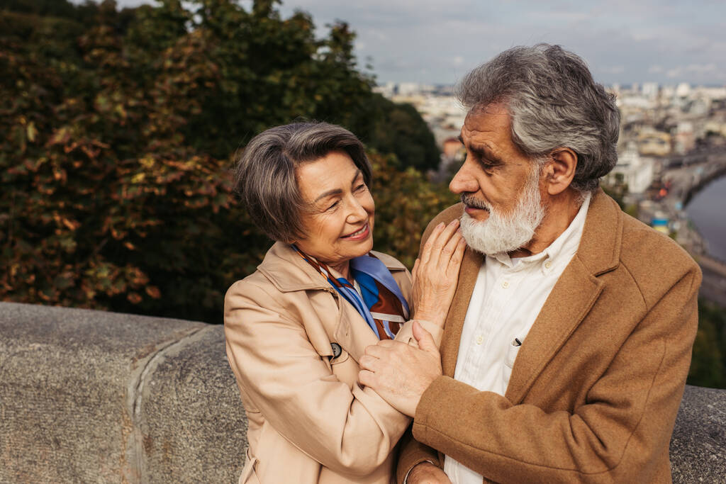 Seniorin stützt sich auf die Schulter ihres Mannes im Mantel, während sie einander ansieht  - Foto, Bild