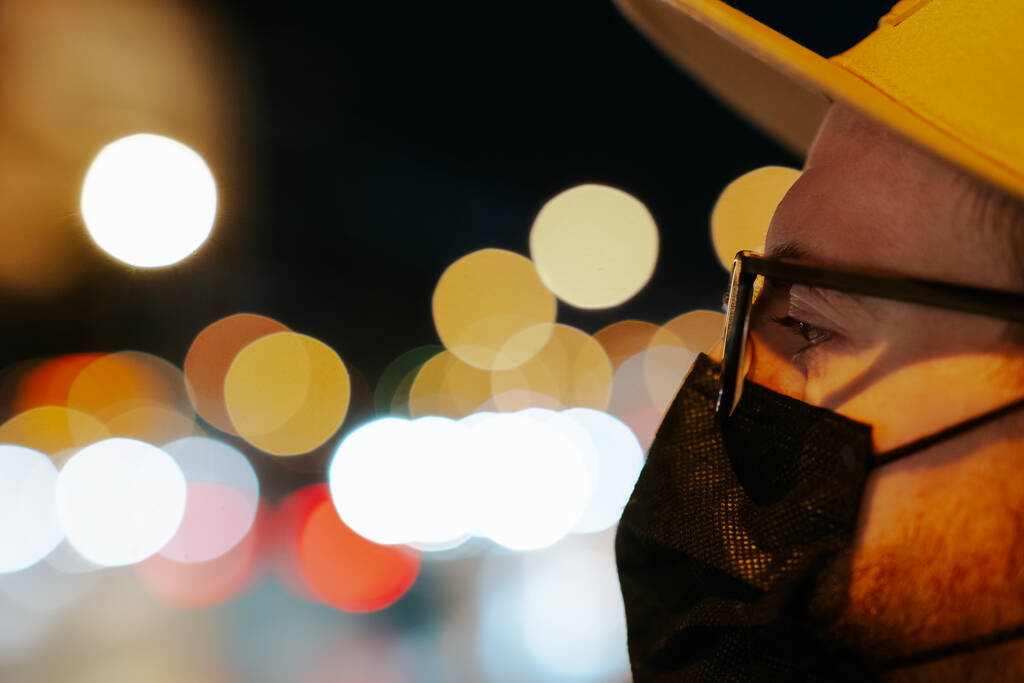 Portret mężczyzny w okularach i masce na twarzy przed światłami bokeh. Nocne ujęcie pieszego z ulicznym bokeh tłem miasta - Zdjęcie, obraz