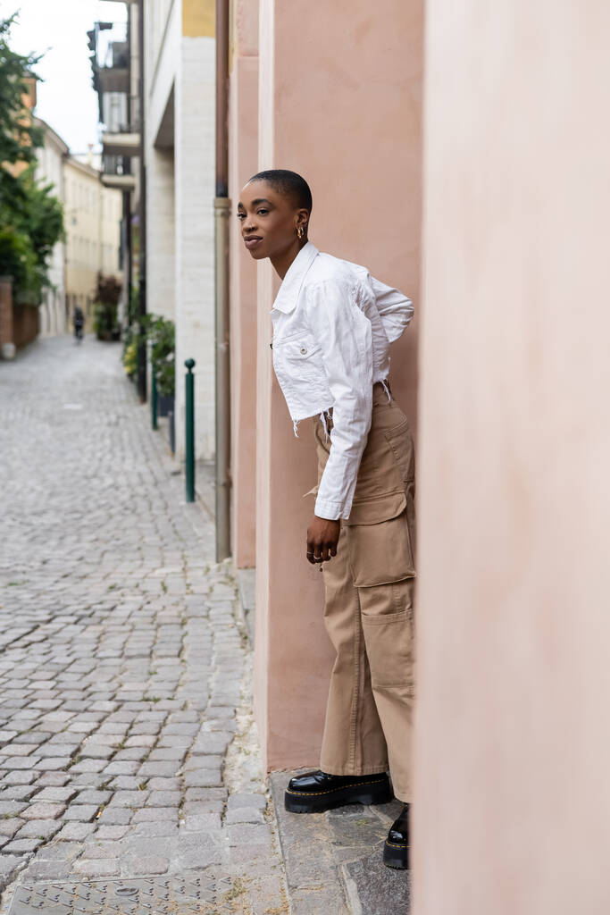 Donna afroamericana alla moda in piedi vicino a edificio su strada urbana a Treviso - Foto, immagini