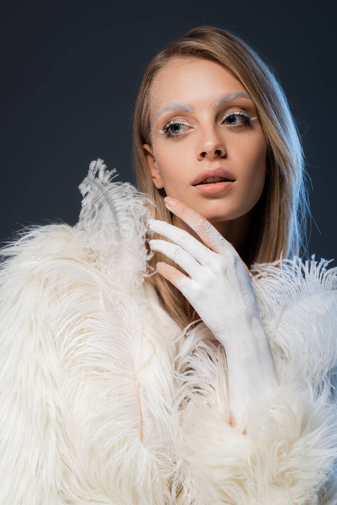 pretty young woman in white faux fur jacket posing with feathers isolated on blue - Photo, Image