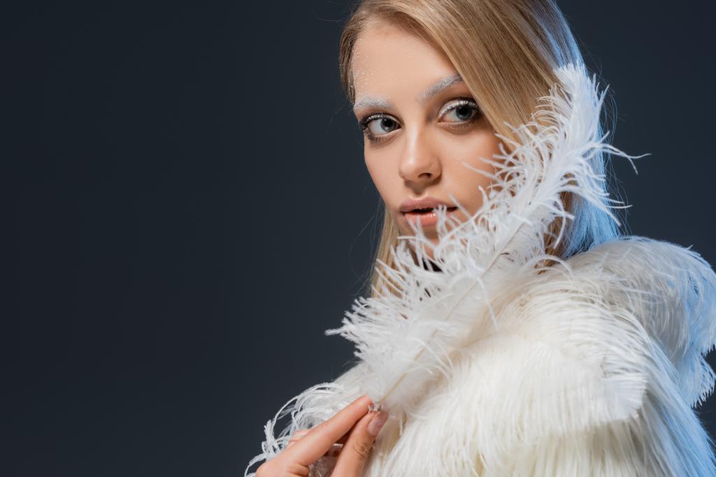 mooie jonge vrouw met winter make-up houden witte veer geïsoleerd op blauw - Foto, afbeelding