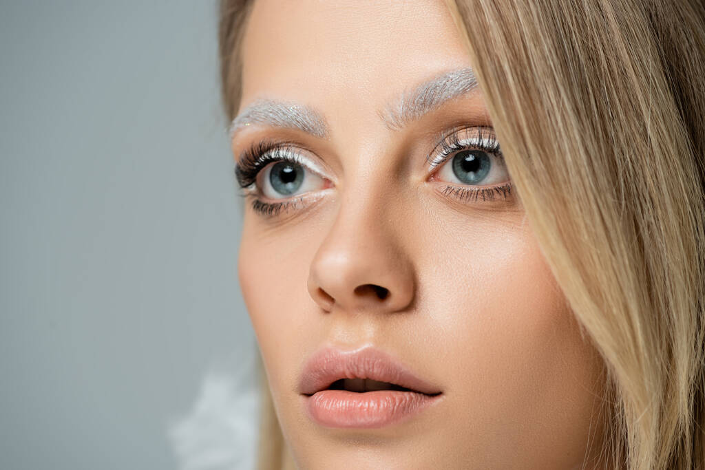 close up view of young model with winter makeup and frozen white eyebrows looking away isolated on grey - Photo, Image