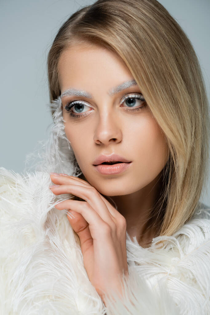 portrait of young woman with winter makeup and white eyebrows posing near white feather isolated on grey - Photo, Image