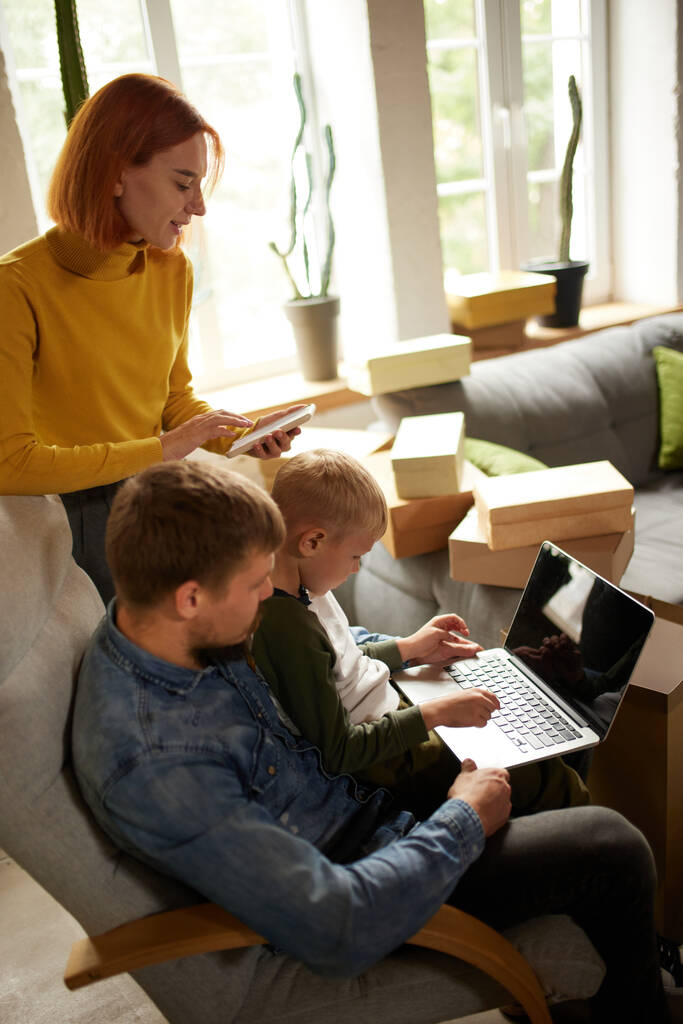 Vásárlás és hétvégék. Fiatal boldog család, szülők és gyerek használja laptop, hogy online rendelés, ellenőrzése vásárlás, vásárlás otthon, beltéri napsütéses őszi napon. Black Friday vagy cyber Monday koncepció - Fotó, kép