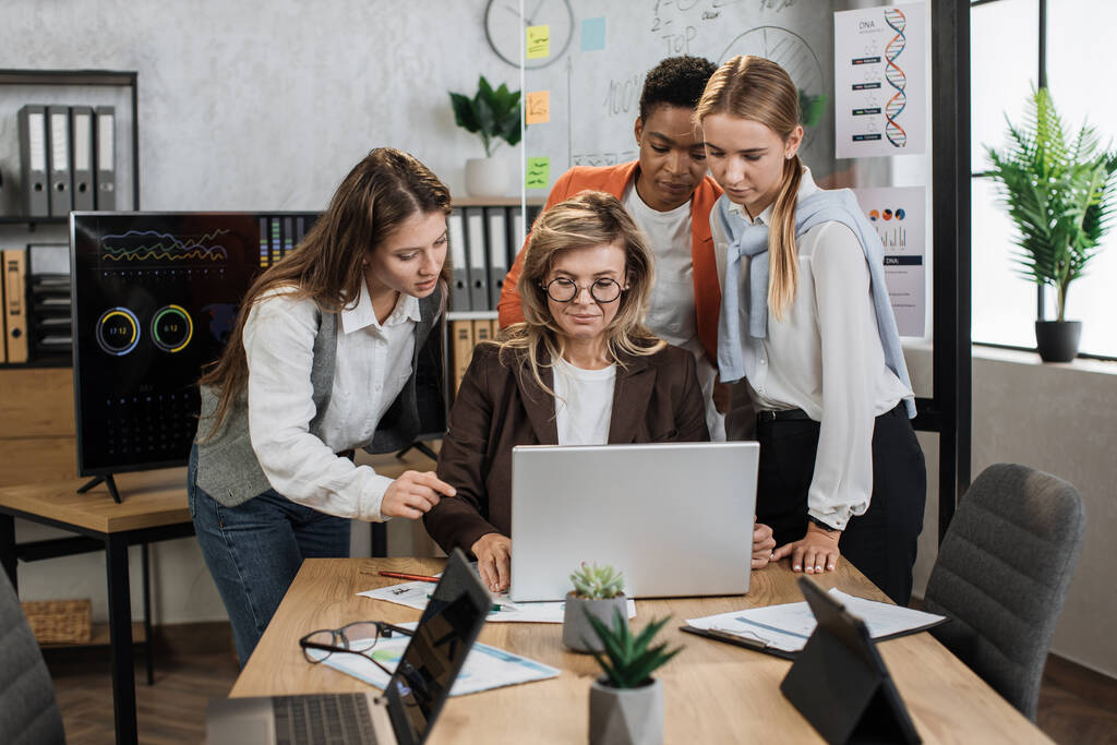 Magabiztos, magasan képzett, multiracionális üzletasszonyok csoportja, akik asztalhoz ülnek és üzleti stratégiáról beszélgetnek, miközben idős hölgy egy laptop-projekten dolgozik.. - Fotó, kép