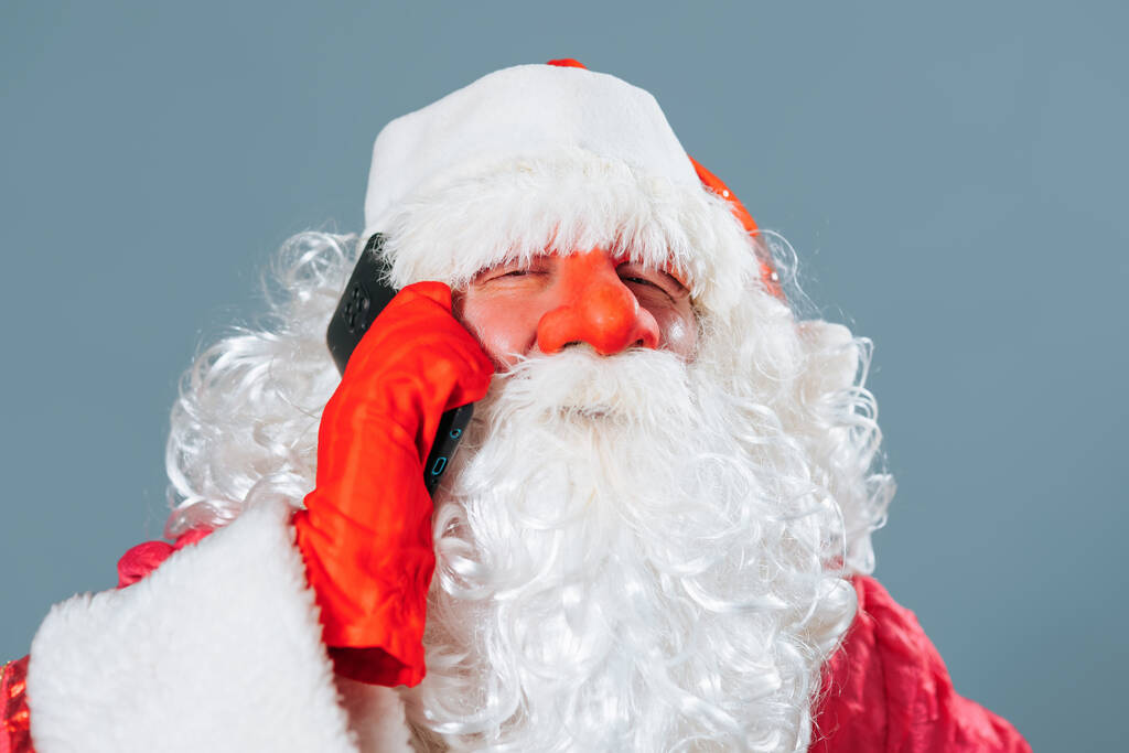 Katse kameraan sinisellä taustalla lähellä edessä näkymä muotokuva Santa Claus puhuu älypuhelimella. Isä Frost päättää tärkeistä asioista joulun ja uudenvuoden aattona.. - Valokuva, kuva