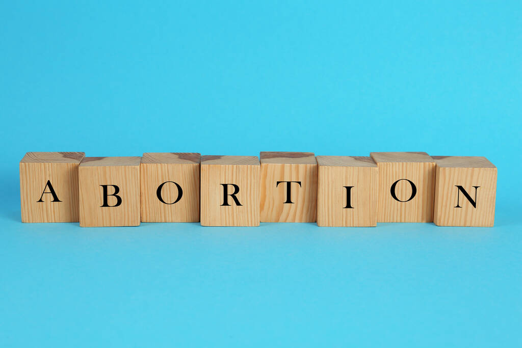 Aborto de palavra feito de cubos de madeira em fundo azul claro - Foto, Imagem