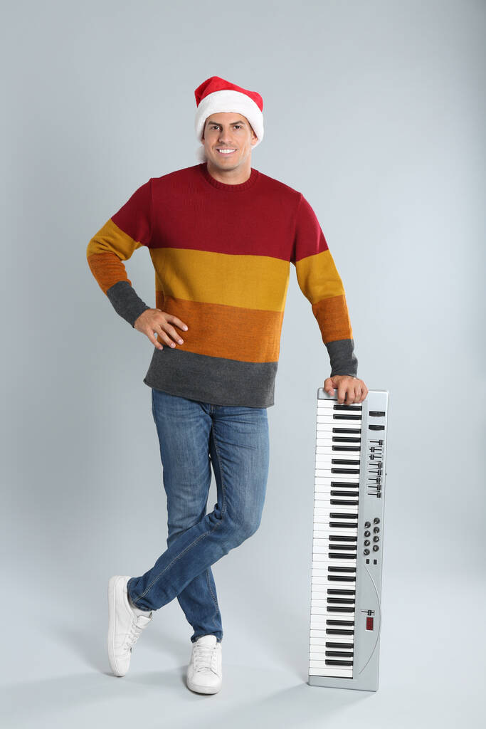 Человек в шляпе Санты с синтезатором на светло-сером фоне. Рождественская музыка - Фото, изображение