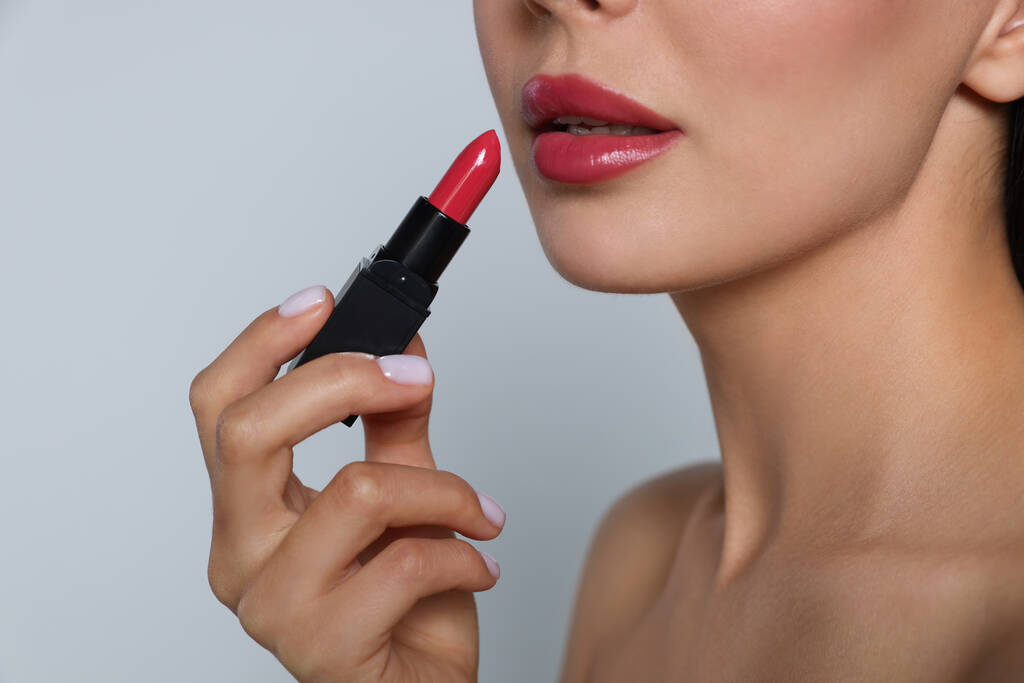 Jeune femme avec un beau maquillage tenant rouge à lèvres brillant sur fond gris clair, gros plan - Photo, image