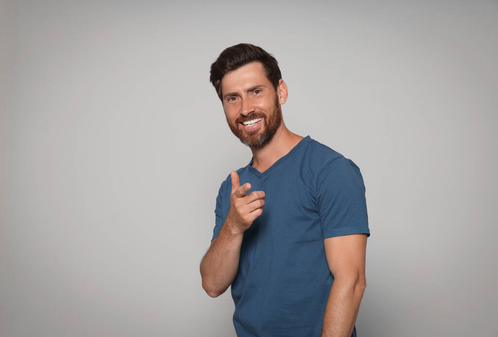 Usmívající se vousatý muž ukazující prstem na šedé pozadí. Mezera pro text - Fotografie, Obrázek