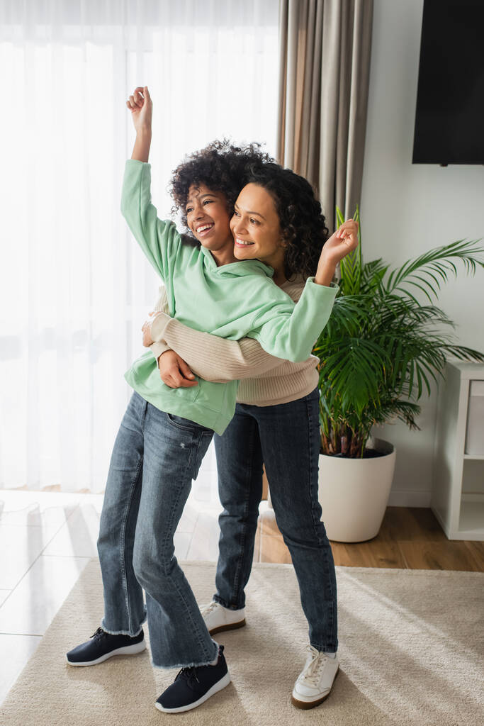 повна довжина весела афроамериканська мати обіймає доньку з піднятими руками
  - Фото, зображення