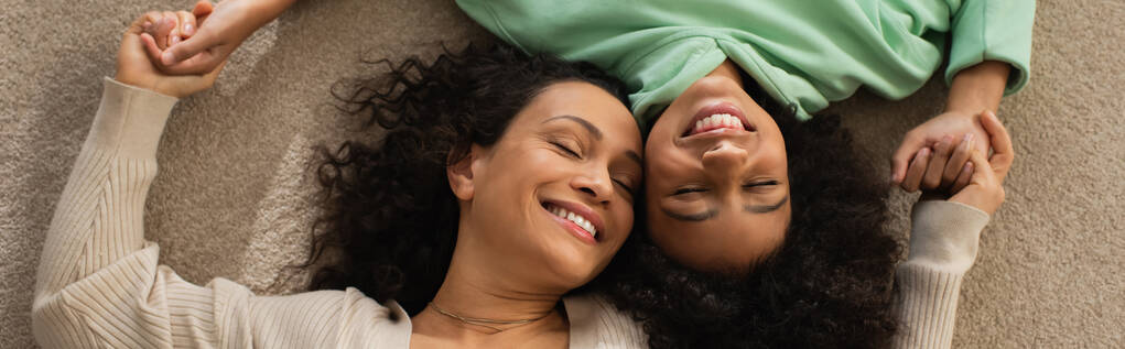 top view of smiling african american girl lying on carpet with cheerful mother, banner - Photo, Image