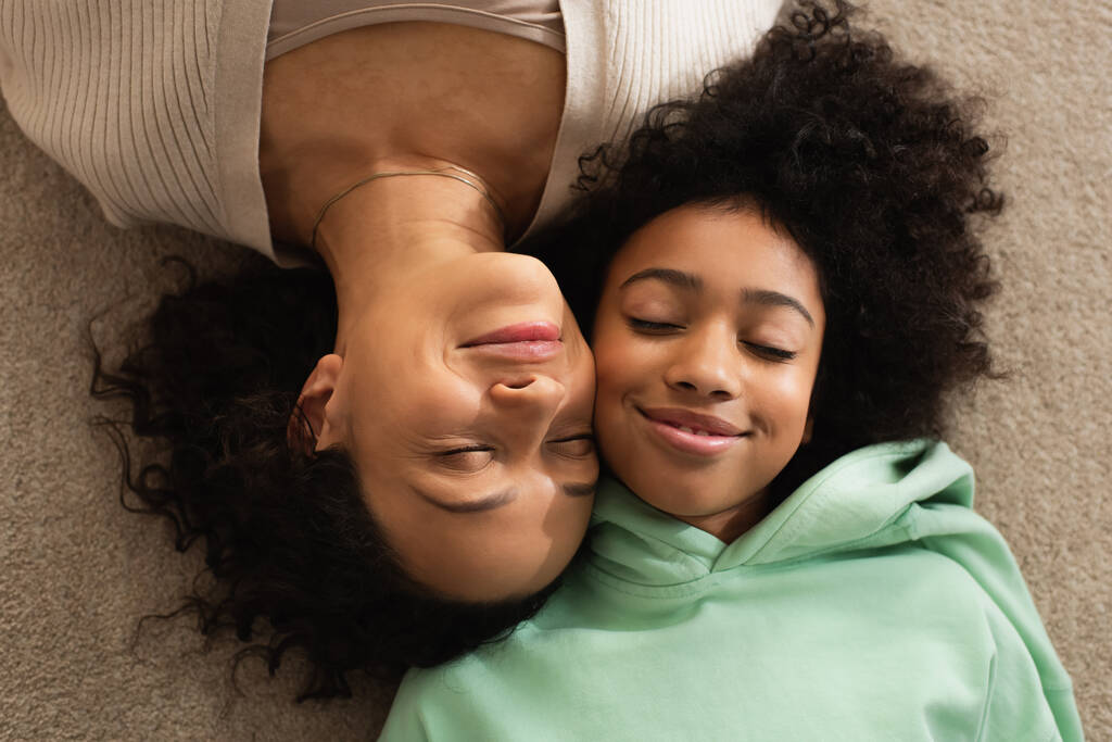 vista superior da menina americana africana feliz deitado no tapete com mãe alegre  - Foto, Imagem