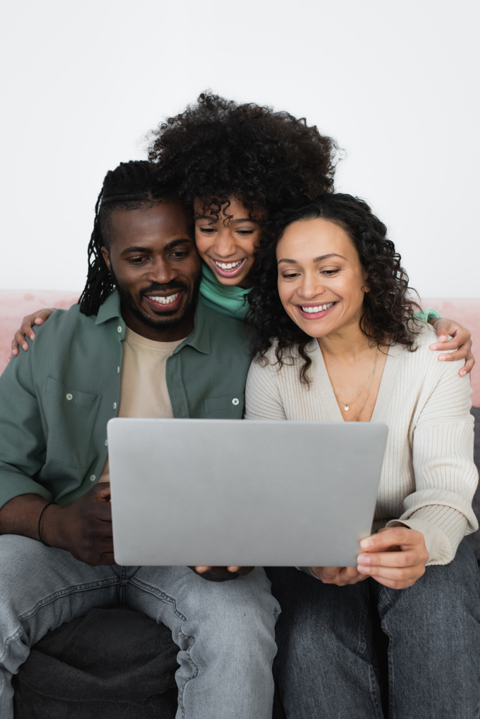 heureux afro-américains parents et préadolescente fille regarder film sur ordinateur portable dans le salon  - Photo, image