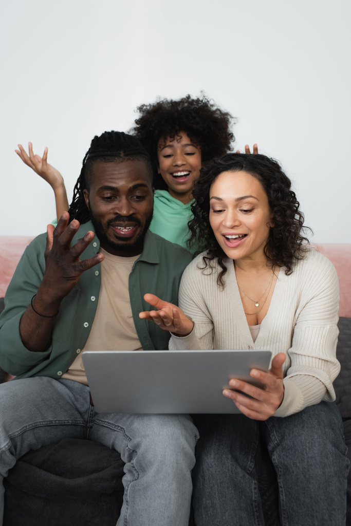 emocjonalny afrykański amerykański rodzina gestykulując podczas oglądania filmu na laptopie w salonie  - Zdjęcie, obraz